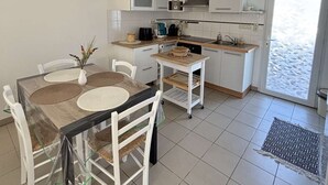 Eine kleine Küche mit weißen Schränken, einem Esstisch mit Stühlen, einer Pendelleuchte und Blick durch eine Glastür.