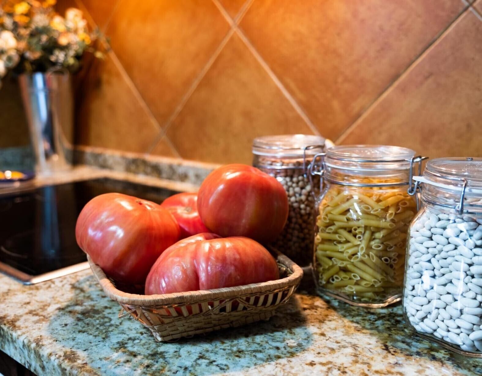 Una encimera de cocina con una cesta de tomates, frascos de pasta y una estufa.