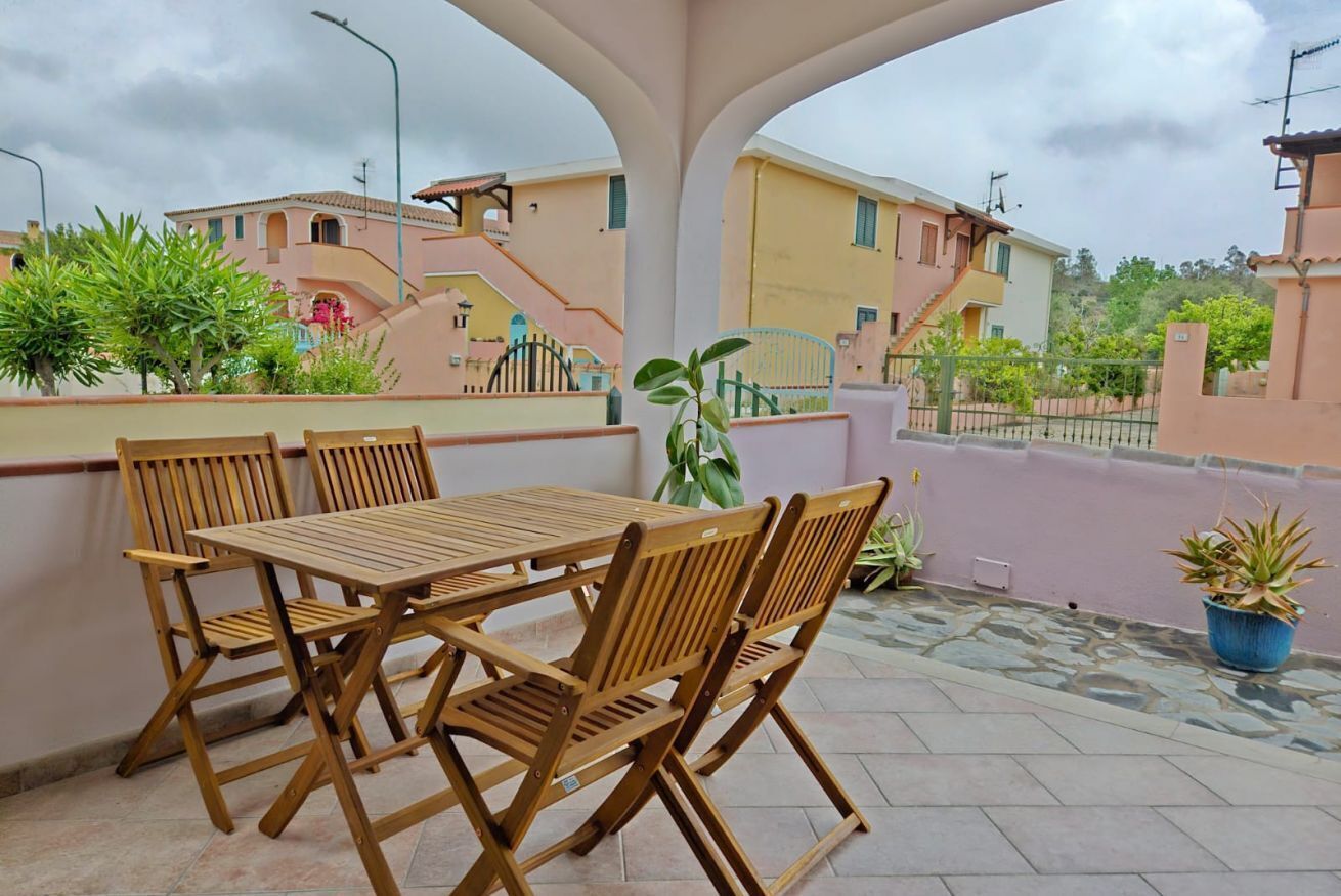 A wooden table and chairs on a balcony with a view of pastel-colored buildings and greenery.