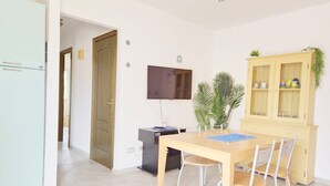 Un coin repas avec une table et des chaises en bois, un téléviseur fixé au mur, un meuble avec des portes en verre et une plante.