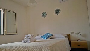 Un lit bien fait, recouvert d’une courtepointe, une lampe de chevet et une pile de serviettes pliées.