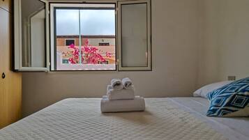 A hotel room with a bed, a window with a view of pink flowers outside, and a towel rack with towels.