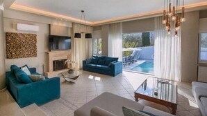 A modern living room with a fireplace, a blue sofa, a glass coffee table, and a view of a pool. - Villa 'Boat' with Sea View, Wi-Fi and Air Conditioning (Ellomeno)