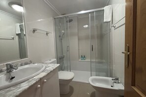 Kylpyhuone, jossa on lasiseinällä varustettu suihku, pesuallas, wc ja bidee.