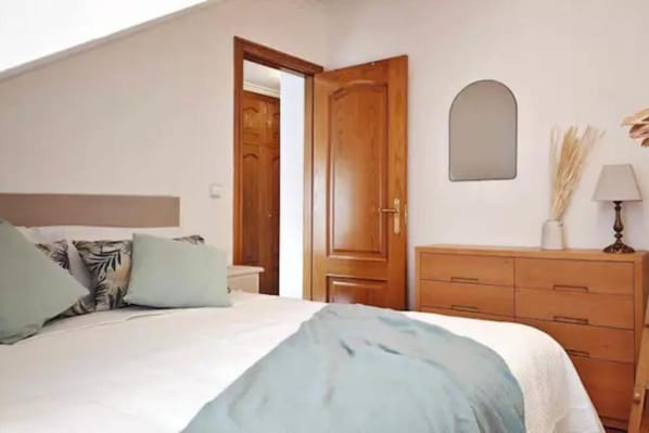 Une chambre à coucher avec un lit, une commode en bois et un miroir au mur.