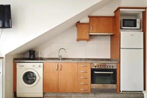 Une cuisine compacte équipée d’un lave-linge, d’un four, d’un four à micro-ondes et de meubles de rangement en bois.