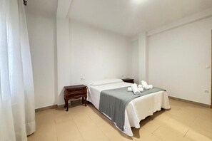 Une chambre simple et épurée, avec un lit, une table de chevet et une petite table en bois.