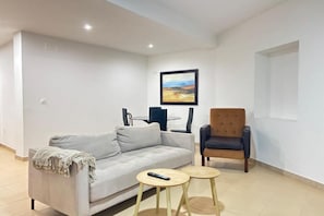 Un salon avec un canapé, deux petites tables, un fauteuil et un tableau accroché au mur.