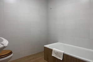 Ein Badezimmer mit weißen Fliesen, einer Holzwc und einer weißen Badewanne mit einem Handtuch.