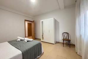 A bedroom with a bed, a wardrobe, a chair, and a door leading to another room.