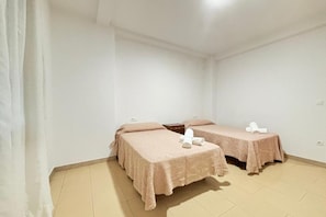 A room with two beds, each with a pink bedspread and pillows, and a small table with a white object on it.
