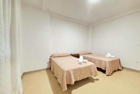 Una habitación con dos camas, cada una con una colcha y almohadas rosadas, y una mesita con un objeto blanco encima.
