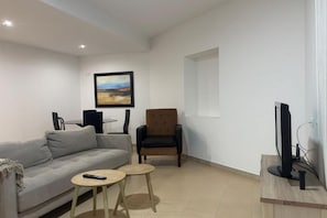 A living room with a sofa, two small tables, a chair, a TV, and a painting on the wall.
