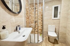A bathroom with a glass-enclosed shower, a white sink with a soap dispenser, and a toilet.