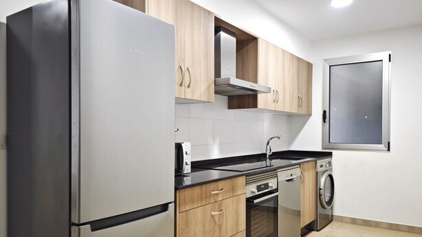 A modern kitchen with stainless steel appliances, wooden cabinets, a built-in oven, and a washing machine. - Desconectaengalicia Carlos Casas Playa Silgar (Sanxenxo)