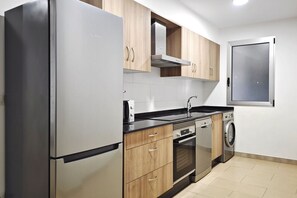 Una cocina moderna con electrodomésticos de acero inoxidable, armarios de madera, horno empotrado y lavadora.
