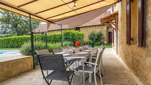 Eine Terrasse im Freien mit Esstisch und Stühlen, im Hintergrund ein Schwimmbecken.