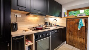 A modern kitchen with dark cabinets, a wooden countertop, a built-in oven, and a window with a view of greenery.