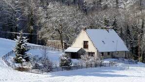 A snow-covered house with a fenced yard, surrounded by trees.