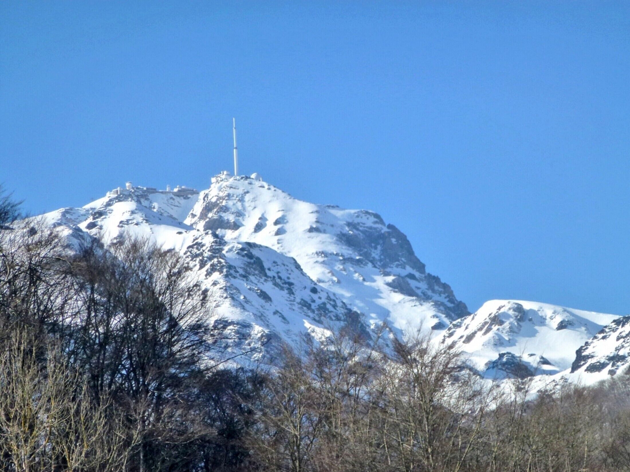 A snow-covered mountain with a tall structure on top, surrounded by trees.