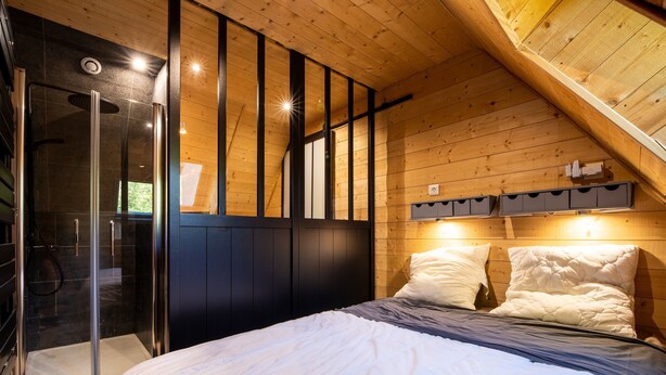 A bedroom with a bed, a wooden ceiling, a glass shower enclosure, and a built-in wardrobe.
