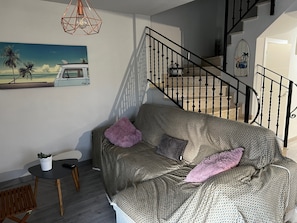 Ein Wohnzimmer mit einer Couch, einem kleinen Tisch, einem Sessel, einem Gemälde und einer Treppe.