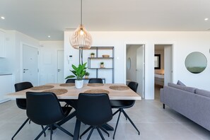 A modern dining area with a wooden table, black chairs, and a hanging light fixture.