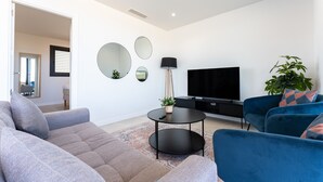 A modern living room with a sofa, armchair, TV, and decorative mirrors. -  Modern Apartment with Sea Views in Higuerón West (Fuengirola)