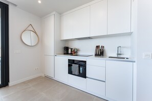 A modern kitchen with white cabinetry, a built-in oven, and a coffee maker.