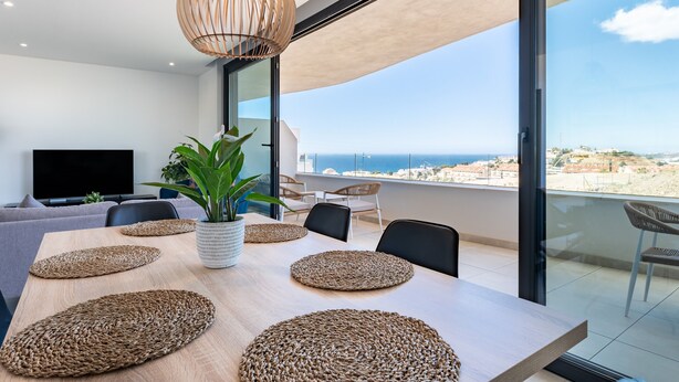 A modern dining area with a large table, woven placemats, a potted plant, and a television. -  Modern Apartment with Sea Views in Higuerón West (Fuengirola)