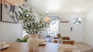 A dining area with a wooden table set for four, surrounded by chairs. A large white vase with greenery is on the table. - Stunning 4BR Modern Gem: Near UW and Green Lake! (Seattle)