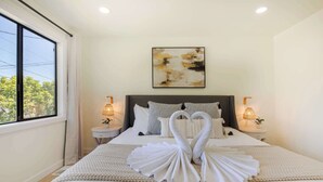 A neatly made bed with two swan-shaped towels, a large abstract painting above the bed, and two bedside lamps on either side. - Stunning 4BR Modern Gem: Near UW and Green Lake! (Seattle)