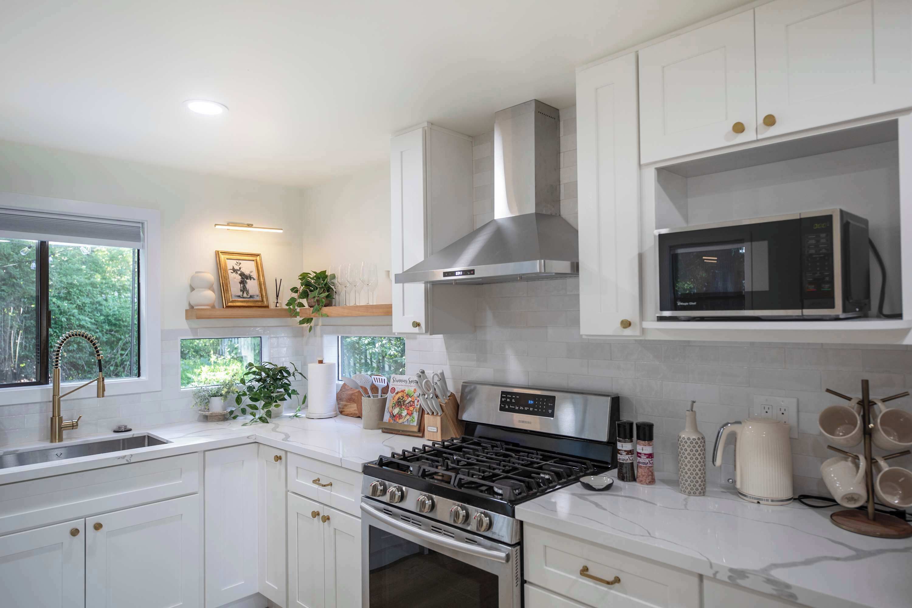 A modern kitchen with white cabinetry, a stainless steel range hood, a microwave, and a gas stove.