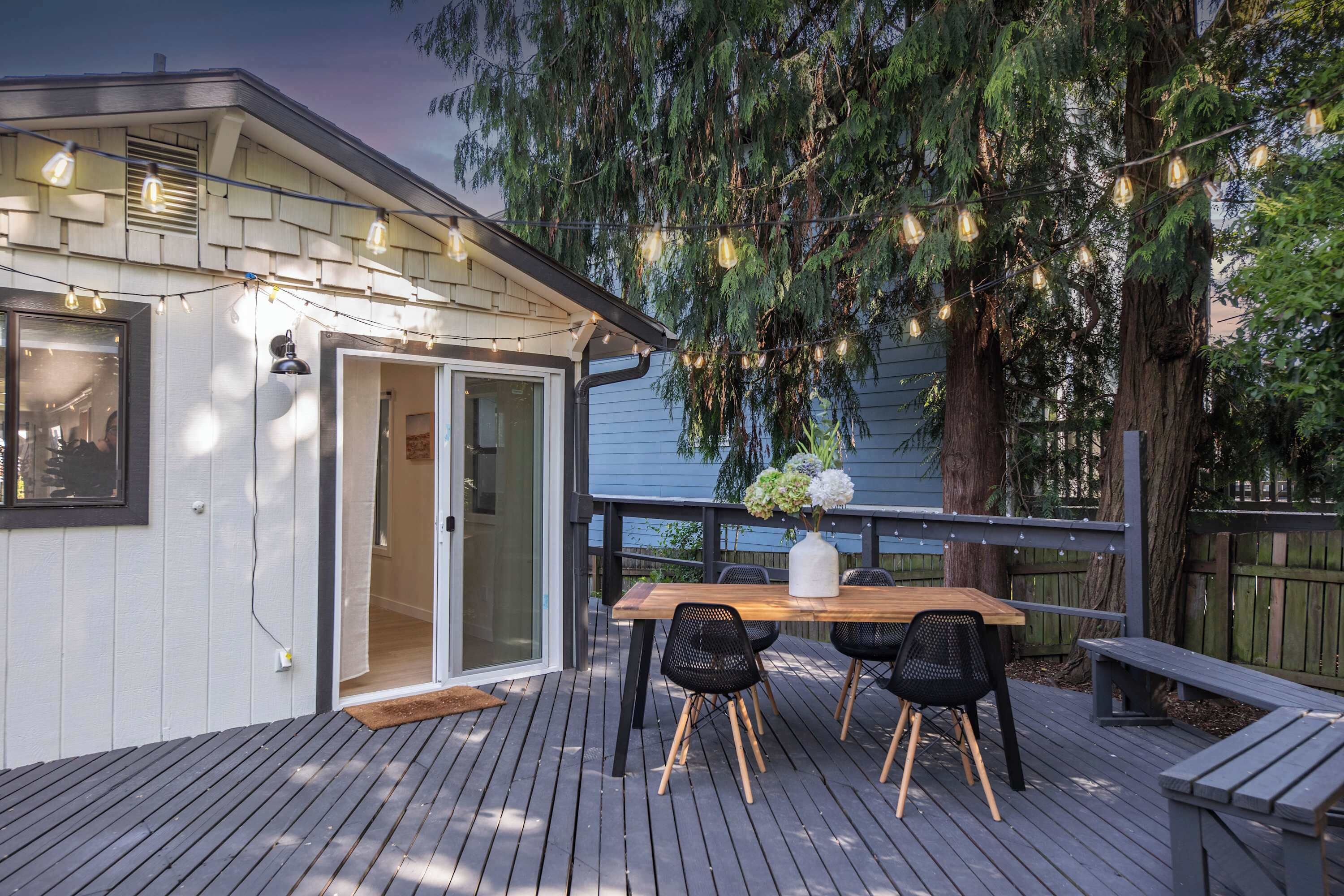 A wooden deck with a table and chairs, a bench, and string lights.