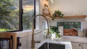 A modern kitchen with a large window, a unique curved faucet, and a wooden shelf with decorative items. - Stunning 4BR Modern Gem: Near UW and Green Lake! (Seattle)