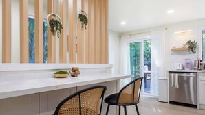 A modern kitchen with a white countertop, two bar stools, a stainless steel refrigerator, and a wooden partition with hanging plants. - Stunning 4BR Modern Gem: Near UW and Green Lake! (Seattle)