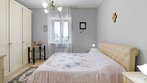 A bedroom with a bed, a nightstand, a dresser, a window with sheer curtains, and a chandelier. - Holiday Home 'Rita Al Vesuvio' with Mountain View, Private Terrace and Private Garden (Terzigno)