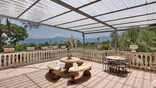 A covered outdoor patio with a table and chairs, a statue, and a view of mountains. - Holiday Home 'Rita Al Vesuvio' with Mountain View, Private Terrace and Private Garden (Terzigno)