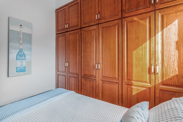 Een slaapkamer met een bed, een houten garderobe en een kunstwerk aan de muur.