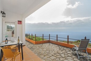 Eine Terrasse mit Steinboden, einem Tisch mit Stühlen, einer Flasche und einem Weinglas.