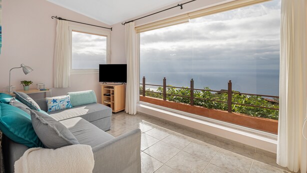 A modern living room with a large window, a flat-screen TV, and a sofa with cushions.