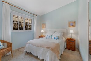 Une chambre à coucher comprenant un lit, deux tables de chevet, une commode, une chaise et une fenêtre avec des rideaux.