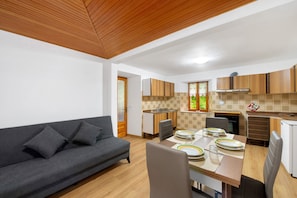 A modern kitchen with wooden cabinets, a dining table set with plates, and a grey sofa in the living area. - Apartment 'Luéisch Ketschu 2' with Mountain View, Shared Garden and Wi-Fi (Issime)