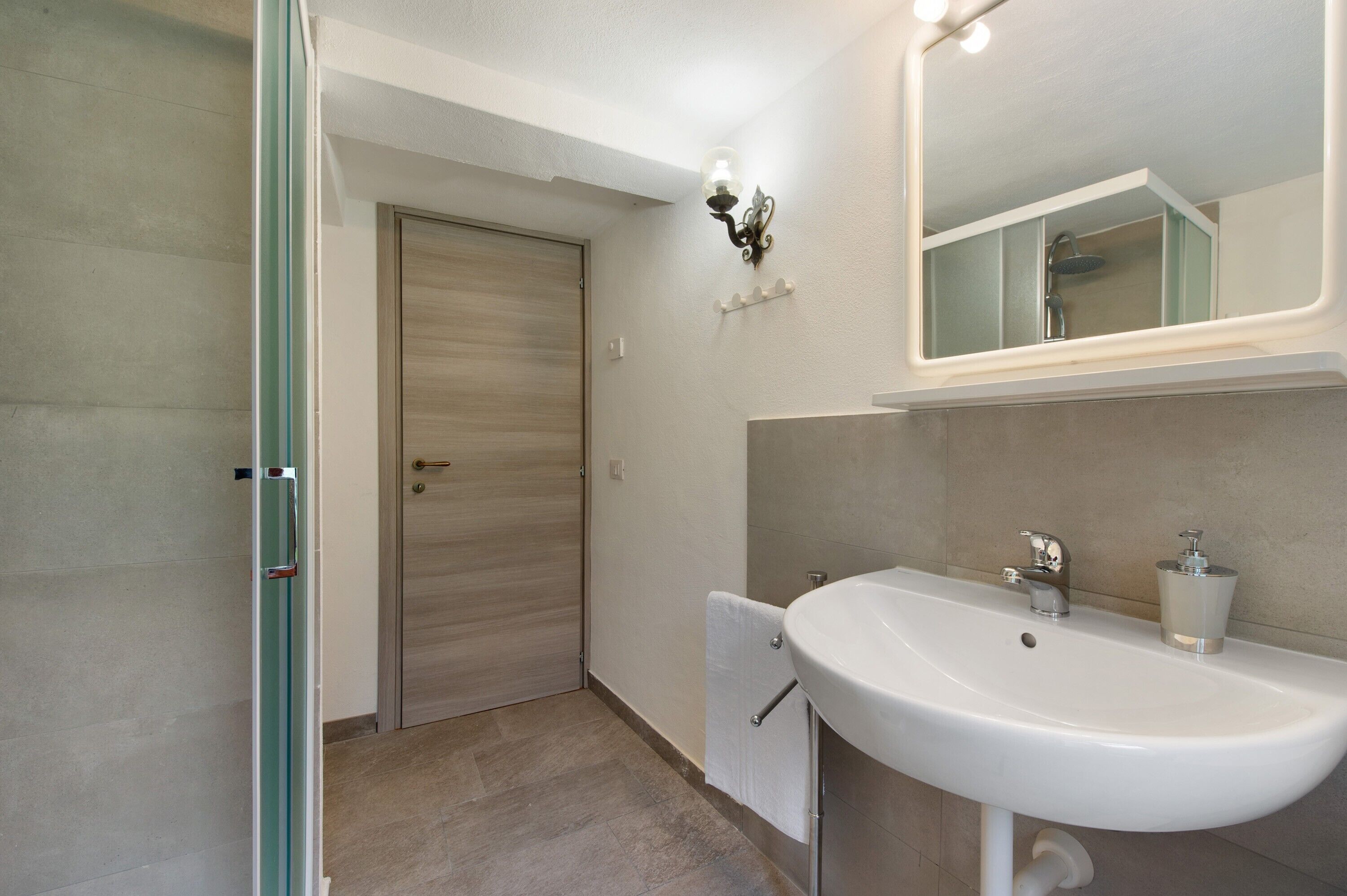Une salle de bain avec un lavabo blanc, un miroir, un porte-serviettes et une porte de douche.