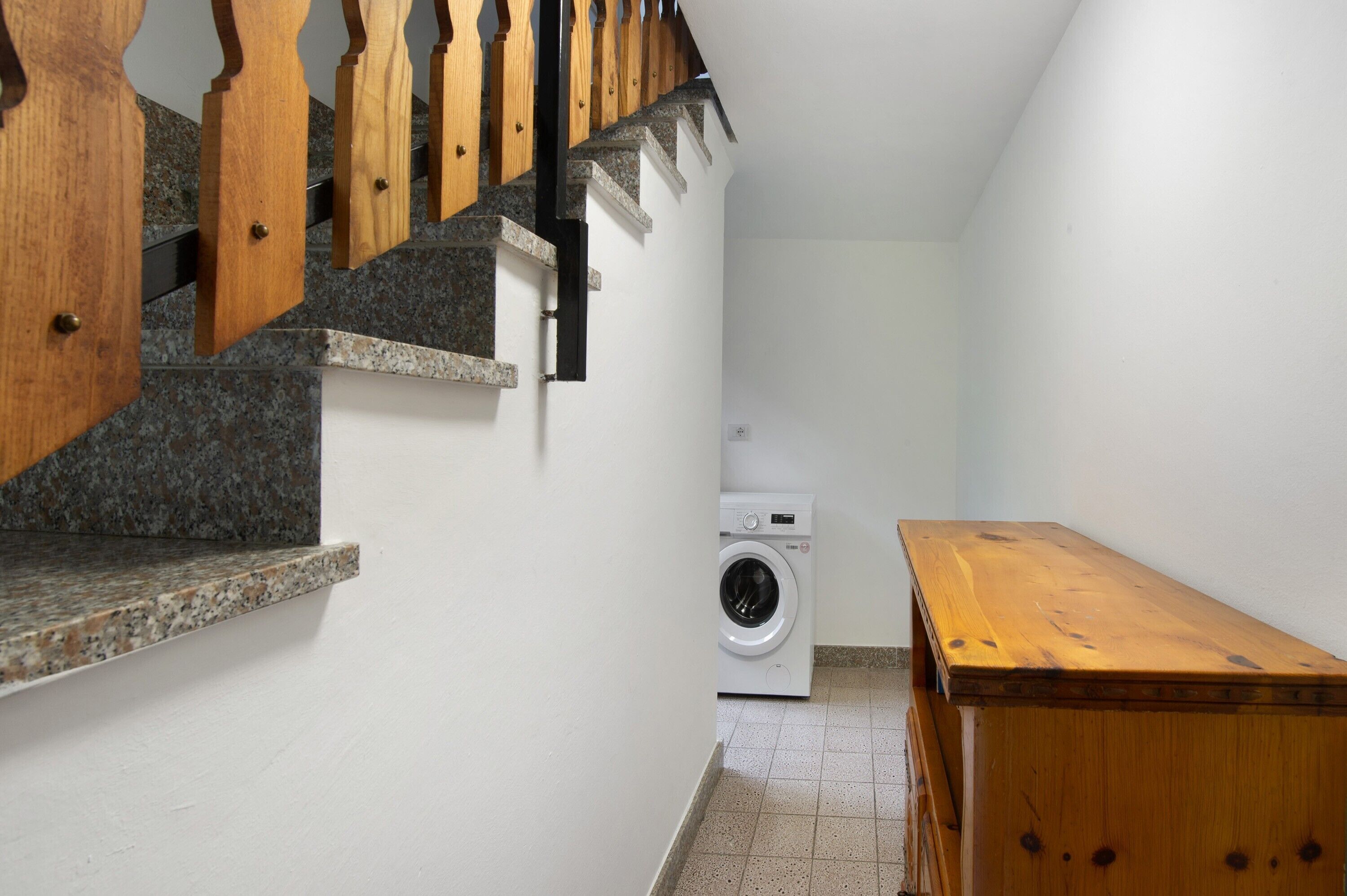 Een wasserette met een wasmachine, een houten bankje en een trap met houten leuningen.