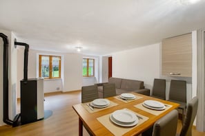 A dining area with a wooden table set for four, a sofa, and a black appliance. - Apartment 'Luéisch Ketschu 1' with Mountain View, Shared Garden and Wi-Fi (Issime)
