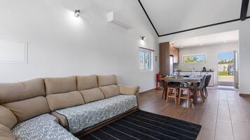 Een moderne woonkamer met een bank, een eethoek met tafel en stoelen, en een keuken die door een open deur zichtbaar is.