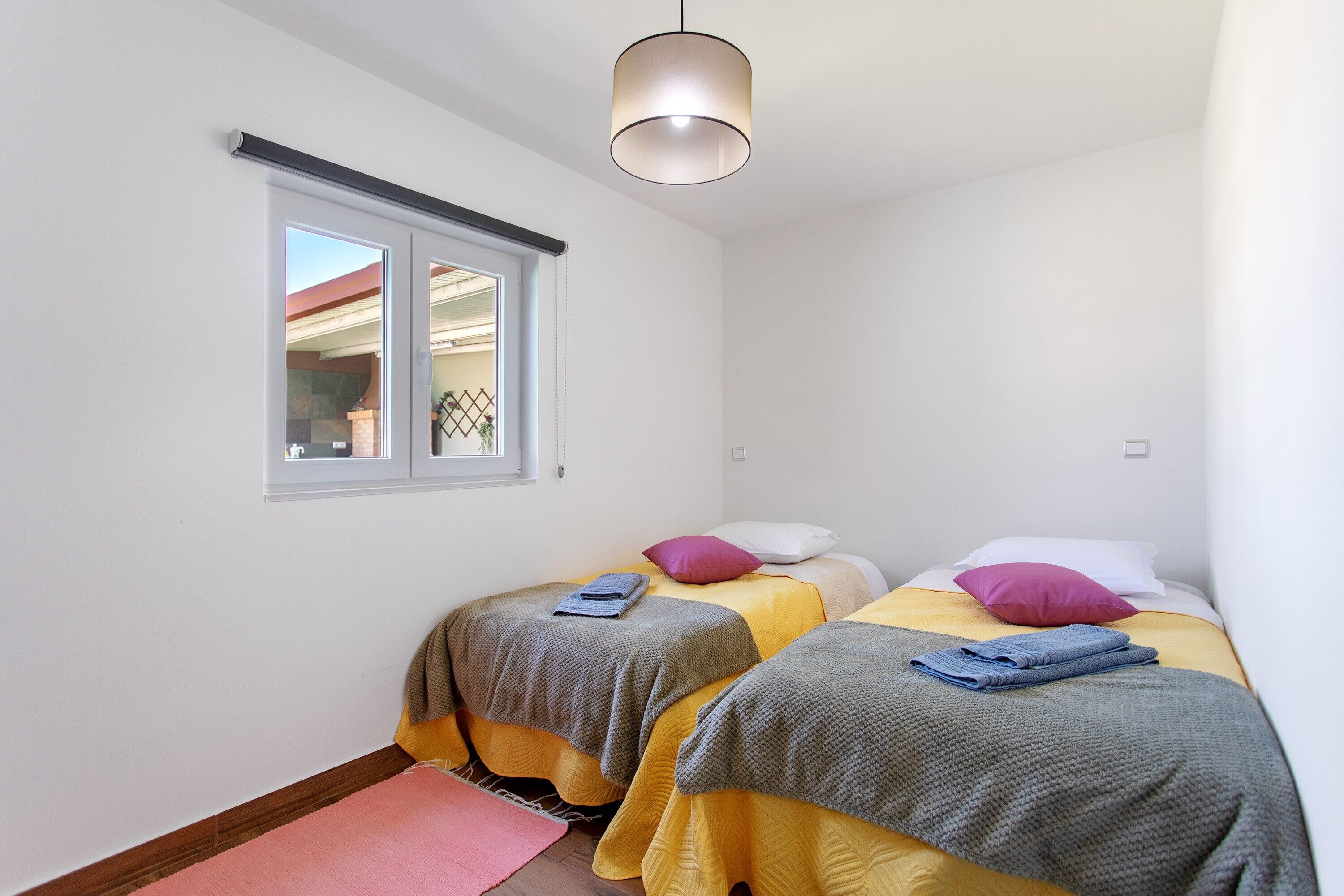 A bedroom with two beds, a window, and a hanging light fixture.