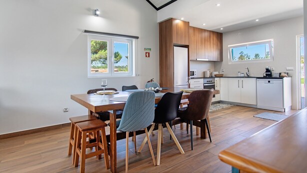 Una cocina moderna con armarios blancos, encimera de madera y una zona de comedor con mesa y sillas de madera.