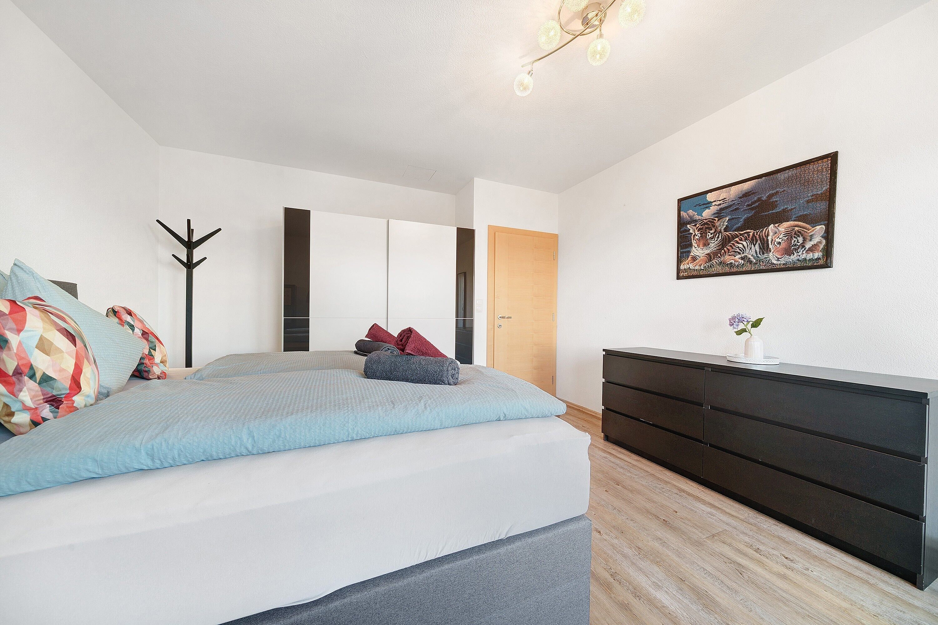 A bedroom with a bed, a dresser, a coat rack, and a painting on the wall.